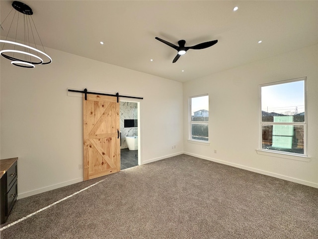 unfurnished bedroom with dark carpet, a barn door, and ensuite bath