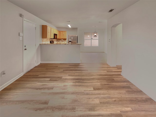 unfurnished living room featuring light wood-type flooring, visible vents, and arched walkways