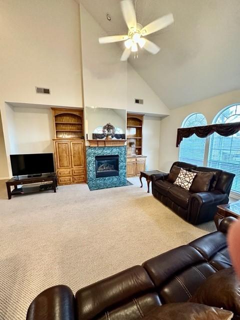 living room with built in shelves, high vaulted ceiling, carpet flooring, and ceiling fan