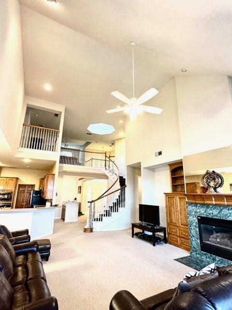 living room featuring a towering ceiling, a high end fireplace, carpet flooring, and ceiling fan