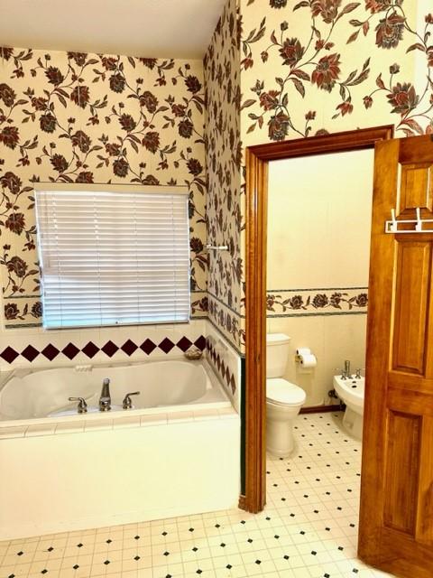 bathroom with a bidet, a tub to relax in, and toilet