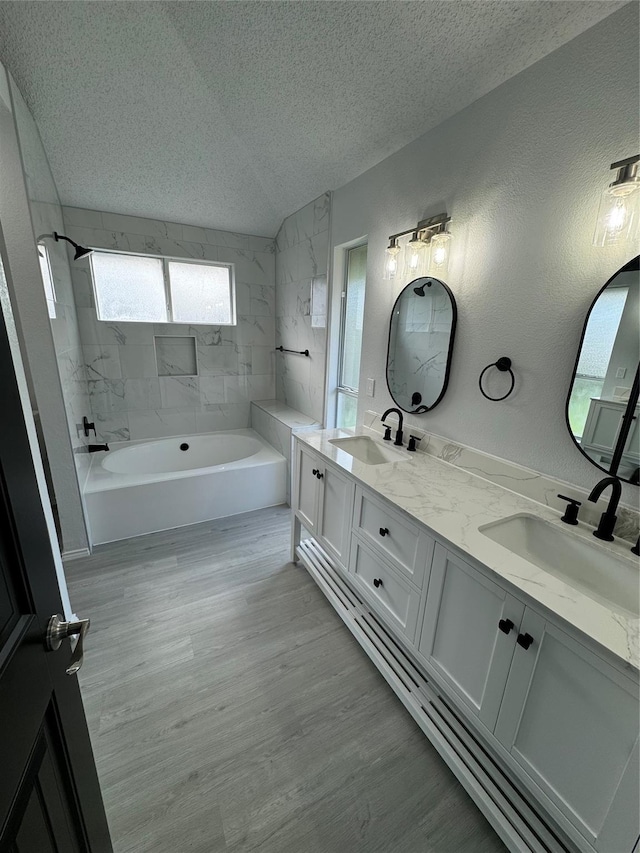 bathroom featuring wood-type flooring, vanity, tiled shower / bath, and a textured ceiling