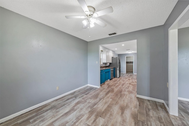 unfurnished living room featuring light hardwood / wood-style floors, ceiling fan, and a textured ceiling