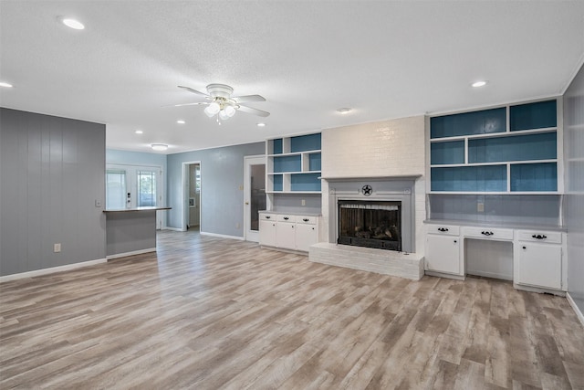 unfurnished living room with built in shelves, a textured ceiling, light hardwood / wood-style floors, ceiling fan, and a fireplace