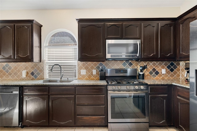 kitchen featuring appliances with stainless steel finishes, dark brown cabinetry, light stone counters, backsplash, and sink