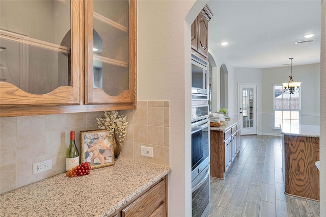 kitchen featuring stainless steel appliances, decorative light fixtures, light stone countertops, a notable chandelier, and tasteful backsplash