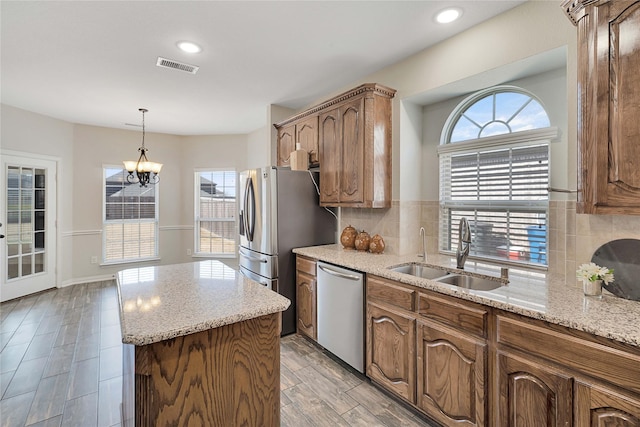 kitchen with appliances with stainless steel finishes, light stone counters, decorative backsplash, a center island, and sink