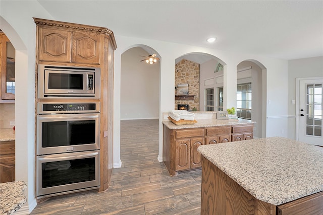 kitchen featuring appliances with stainless steel finishes, light stone countertops, a center island, and a stone fireplace