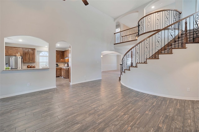 unfurnished living room with a high ceiling, dark wood-type flooring, and ceiling fan