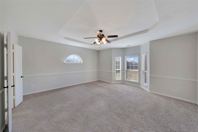 empty room with a raised ceiling, light carpet, and ceiling fan