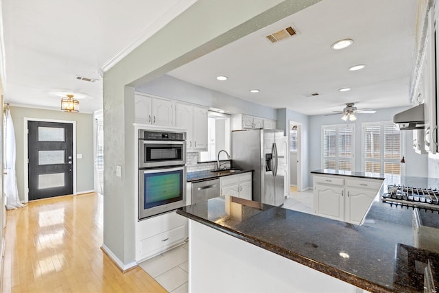 kitchen featuring appliances with stainless steel finishes, extractor fan, white cabinetry, kitchen peninsula, and tasteful backsplash