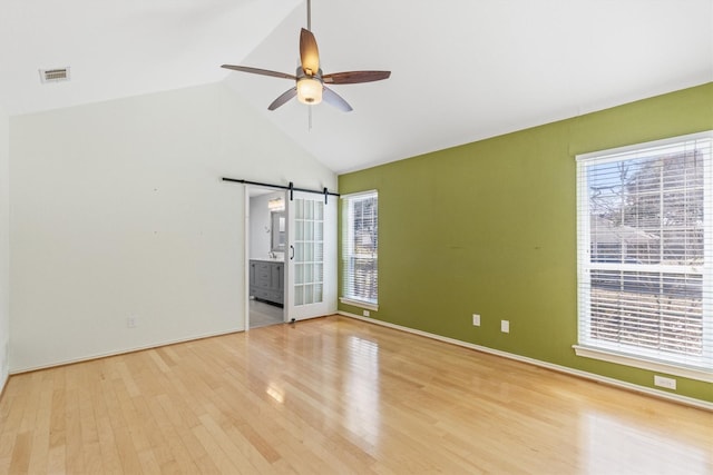 empty room featuring light hardwood / wood-style floors, high vaulted ceiling, ceiling fan, and a barn door