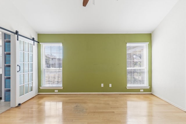 spare room with ceiling fan, light hardwood / wood-style flooring, and a barn door