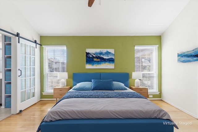 bedroom with a barn door, ceiling fan, and wood-type flooring