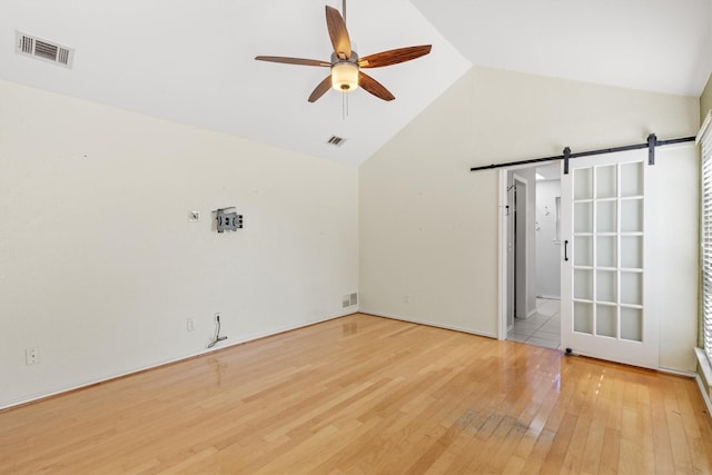 unfurnished room with light hardwood / wood-style floors, high vaulted ceiling, ceiling fan, and a barn door