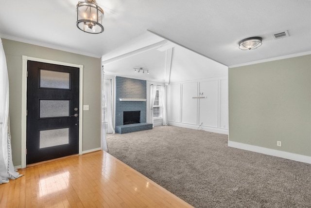 entryway featuring carpet floors, a chandelier, crown molding, and a brick fireplace