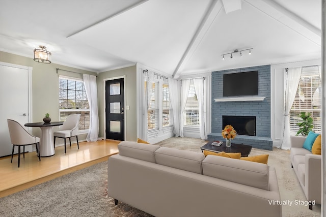 living room featuring ornamental molding, a brick fireplace, lofted ceiling with beams, and a healthy amount of sunlight