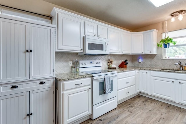 kitchen featuring white appliances, light stone counters, white cabinets, light hardwood / wood-style floors, and sink