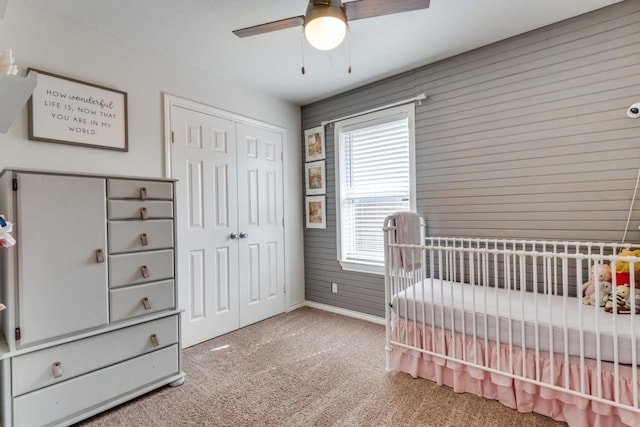 carpeted bedroom featuring a closet, ceiling fan, and a nursery area