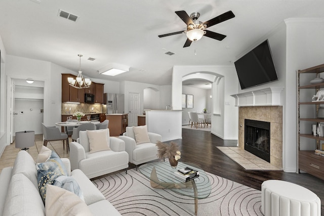 living room featuring ceiling fan with notable chandelier, light hardwood / wood-style floors, and a tile fireplace