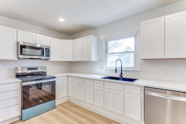 kitchen featuring light wood-type flooring, stainless steel appliances, sink, backsplash, and white cabinets