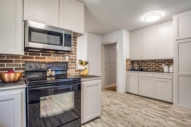 kitchen with light hardwood / wood-style flooring, black electric range oven, white cabinets, and decorative backsplash