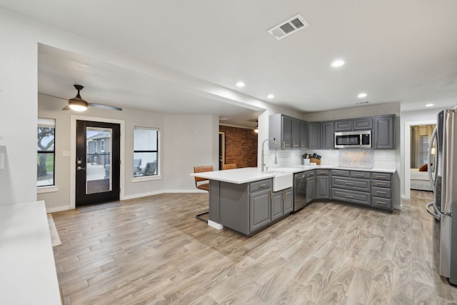 kitchen with a peninsula, stainless steel appliances, gray cabinets, and light countertops