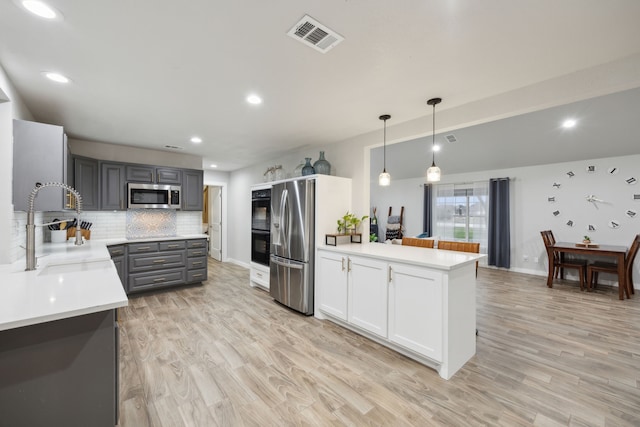 kitchen with pendant lighting, stainless steel appliances, light countertops, visible vents, and gray cabinetry