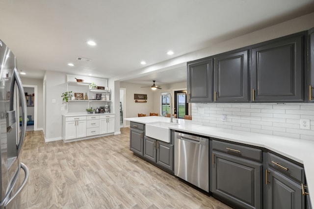 kitchen with a sink, light countertops, appliances with stainless steel finishes, decorative backsplash, and light wood finished floors