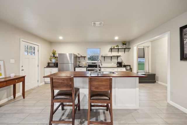 kitchen featuring visible vents, wooden counters, freestanding refrigerator, a sink, and black microwave