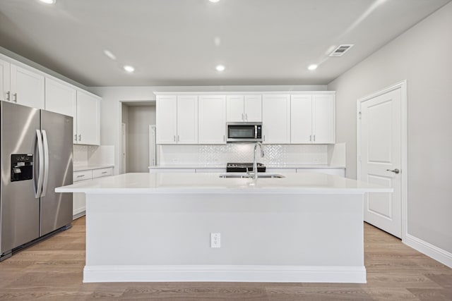 kitchen with stainless steel appliances, light countertops, a center island with sink, and white cabinetry