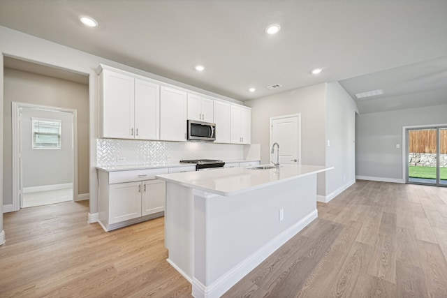 kitchen with stainless steel appliances, light countertops, white cabinetry, and an island with sink