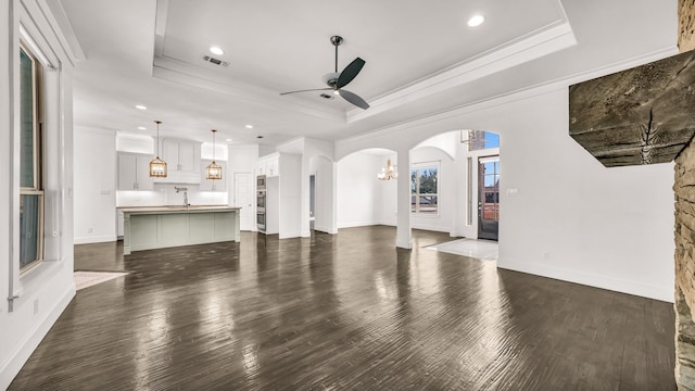 114 N Star Crossing Ln, Weatherford, TX 76088 - unfurnished living room featuring ceiling fan with notable chandelier, a raised ceiling, arched walkways, ornamental molding, and dark wood-style floors