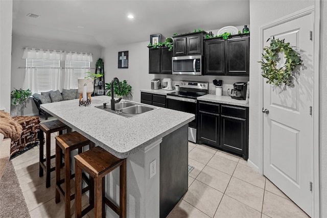 kitchen with appliances with stainless steel finishes, a breakfast bar area, light tile patterned floors, sink, and a kitchen island with sink