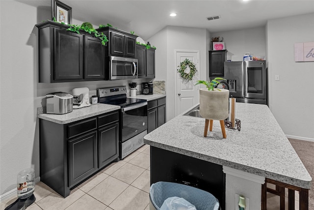 kitchen with a kitchen breakfast bar, light tile patterned floors, stainless steel appliances, and an island with sink