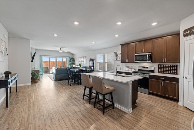 kitchen featuring a center island with sink, light hardwood / wood-style flooring, sink, appliances with stainless steel finishes, and a kitchen bar