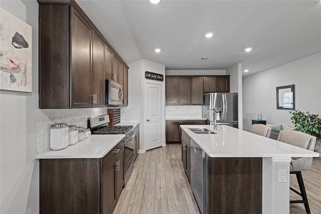 kitchen with an island with sink, a breakfast bar, light hardwood / wood-style flooring, sink, and appliances with stainless steel finishes