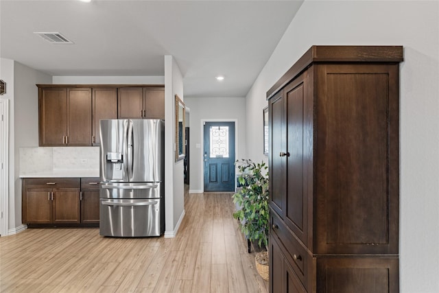 kitchen featuring light wood-type flooring, dark brown cabinetry, tasteful backsplash, and stainless steel fridge