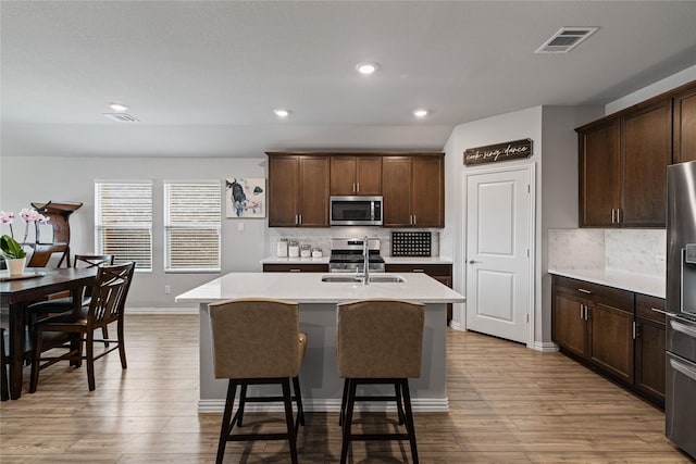 kitchen with appliances with stainless steel finishes, light wood-type flooring, an island with sink, and backsplash