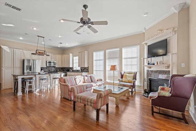 living room with light hardwood / wood-style flooring, a tile fireplace, ceiling fan, ornamental molding, and sink