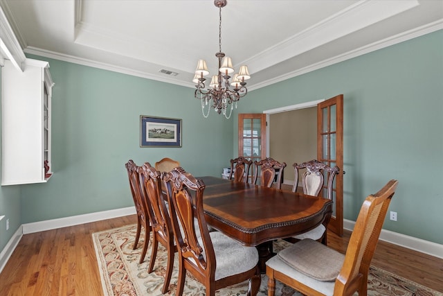 dining area with a tray ceiling, ornamental molding, hardwood / wood-style flooring, and an inviting chandelier