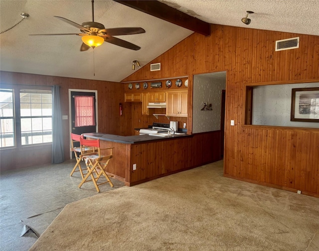 kitchen featuring electric range oven, kitchen peninsula, wood walls, vaulted ceiling with beams, and a textured ceiling