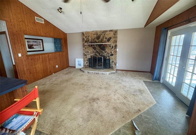 unfurnished living room featuring french doors, lofted ceiling, wood walls, and a stone fireplace