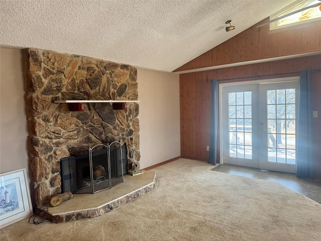 unfurnished living room featuring french doors, carpet floors, a stone fireplace, vaulted ceiling, and a textured ceiling