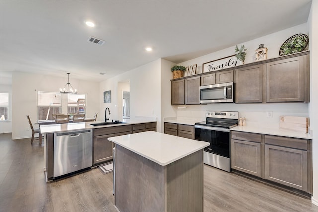 kitchen featuring light wood-type flooring, kitchen peninsula, hanging light fixtures, stainless steel appliances, and sink