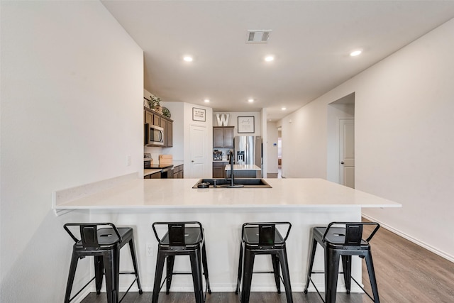 kitchen with kitchen peninsula, hardwood / wood-style flooring, stainless steel appliances, a breakfast bar, and sink