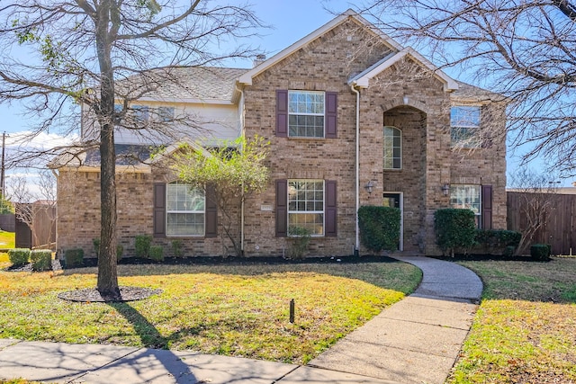 traditional-style home with brick siding, a front lawn, and fence