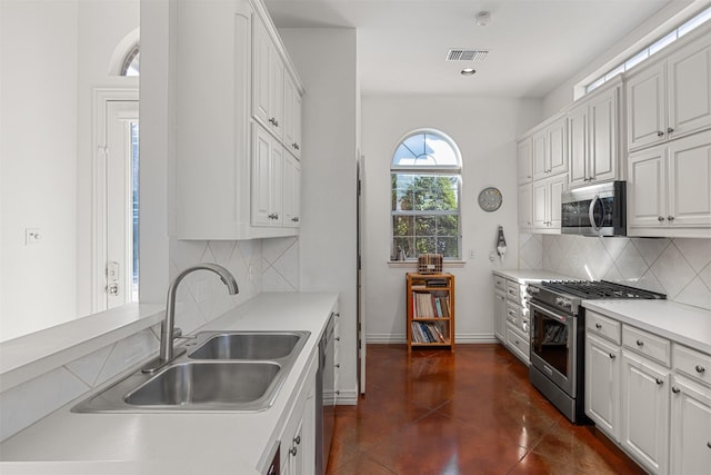 kitchen with appliances with stainless steel finishes, sink, backsplash, white cabinetry, and dark tile patterned flooring