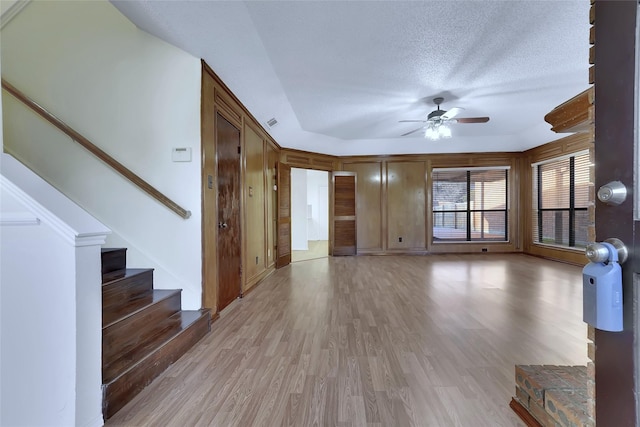 unfurnished living room with visible vents, a ceiling fan, a textured ceiling, light wood-type flooring, and stairs