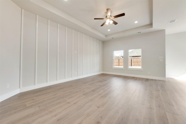 empty room with ceiling fan, light wood-type flooring, and a raised ceiling